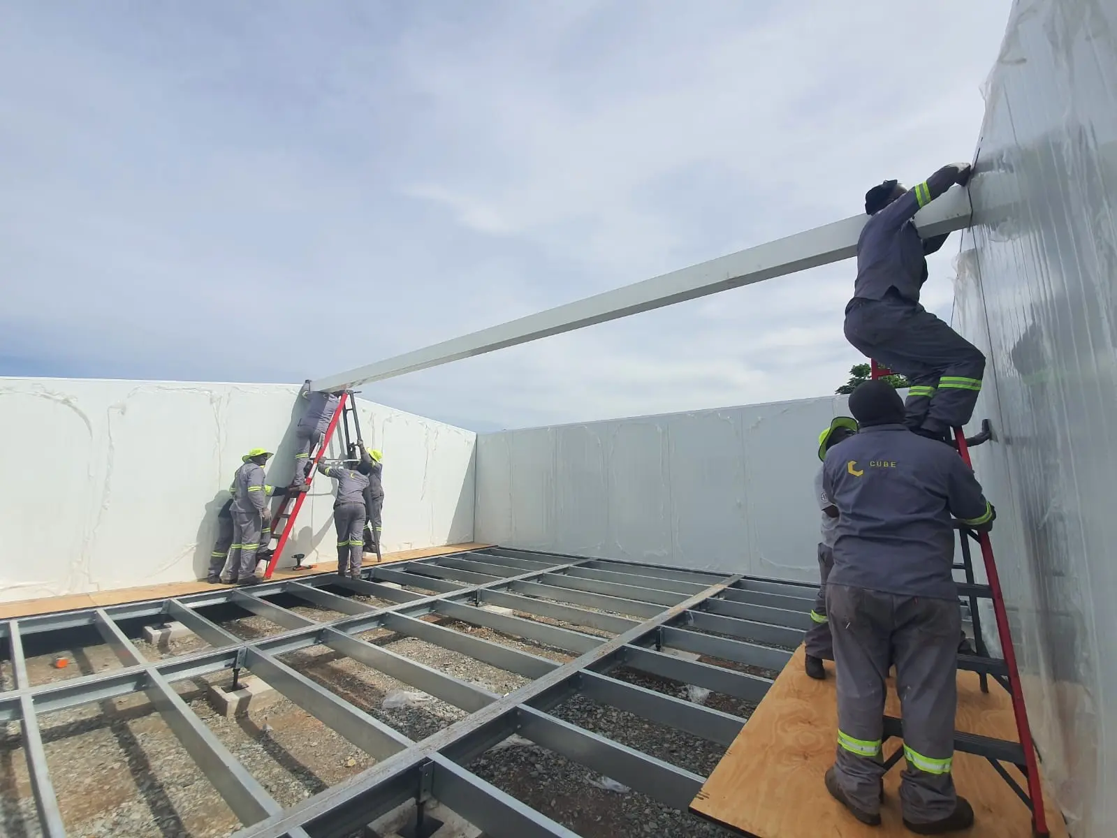 A site crew positioning a roof panel over a steel floor frame